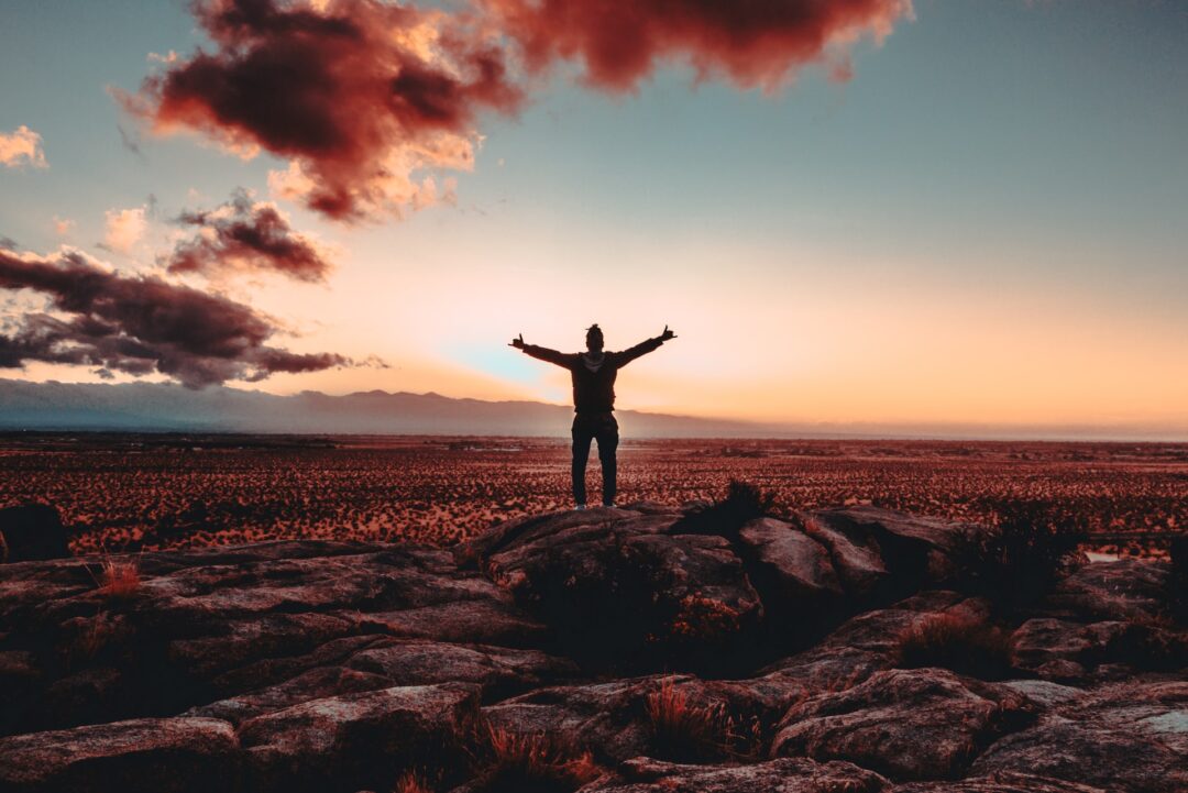 PERSON STARND ON A ROCK RAISING BOTH HAND